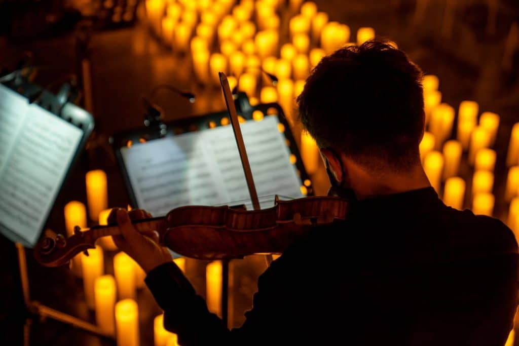 A man playing the violin with candles in front of him and sheet music.