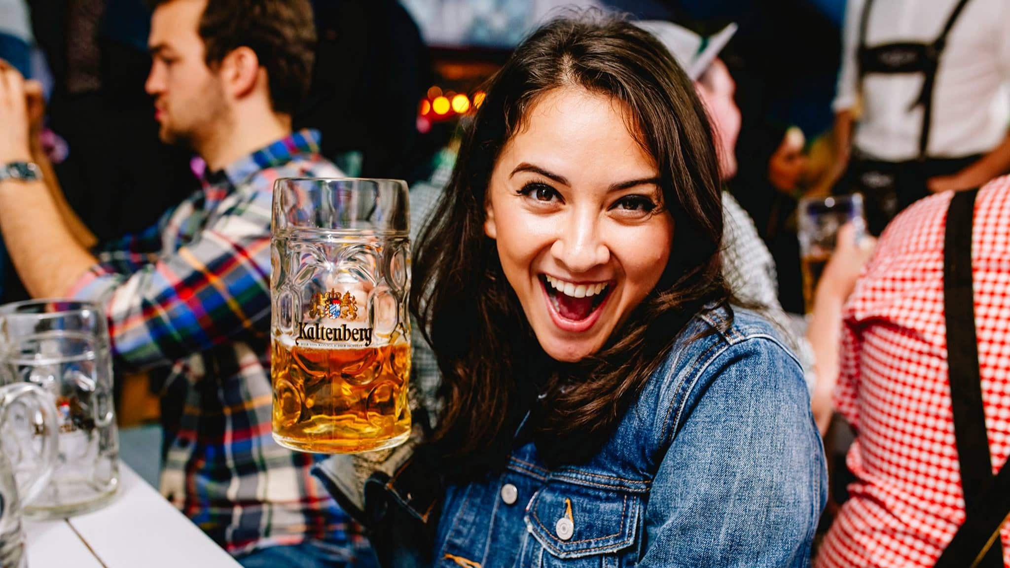 A woman holding up a stein of beer for Oktoberfest and smiling at the camera
