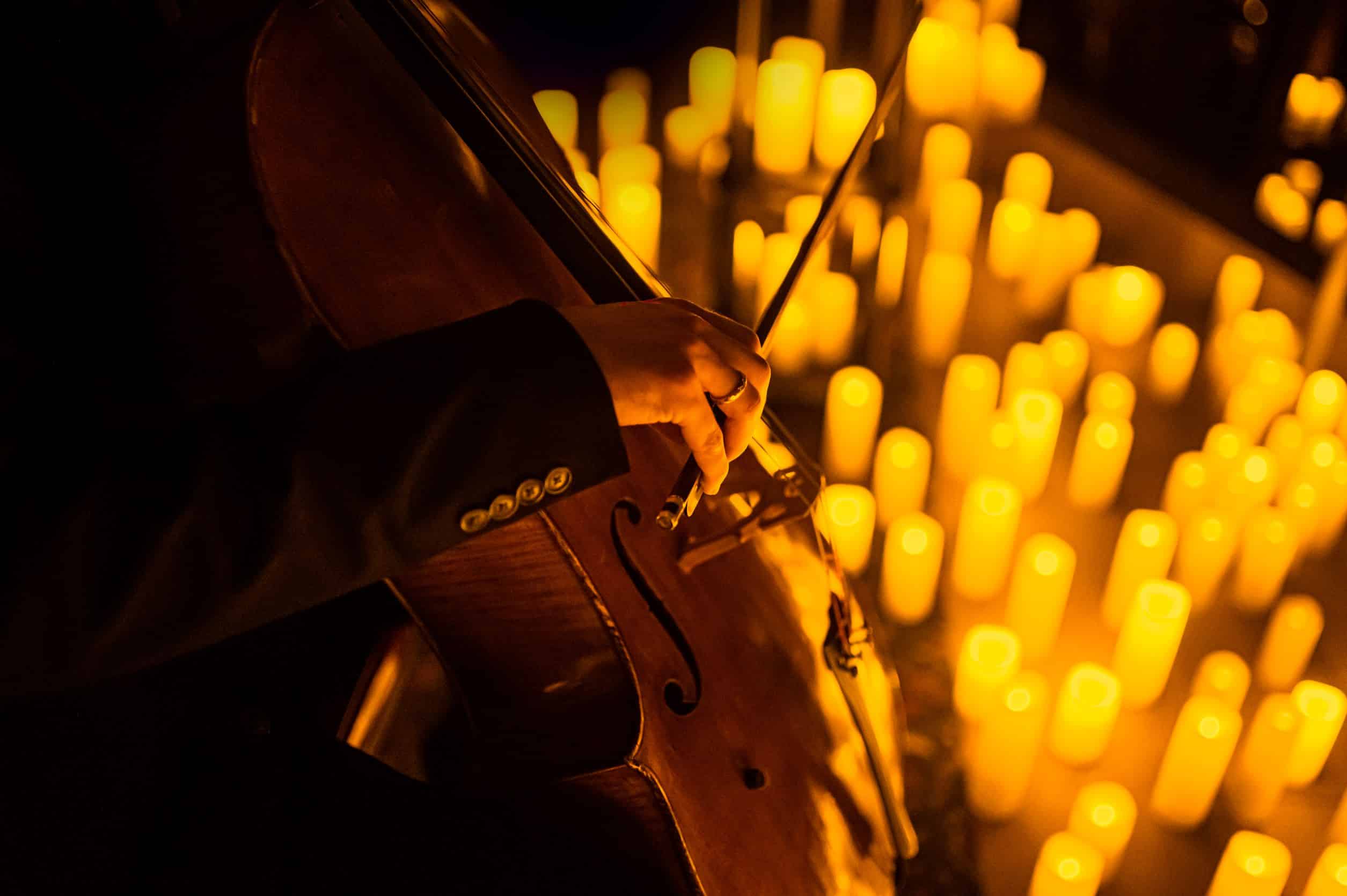 A hand playing the cello with candles in the background at a Candlelight concert.