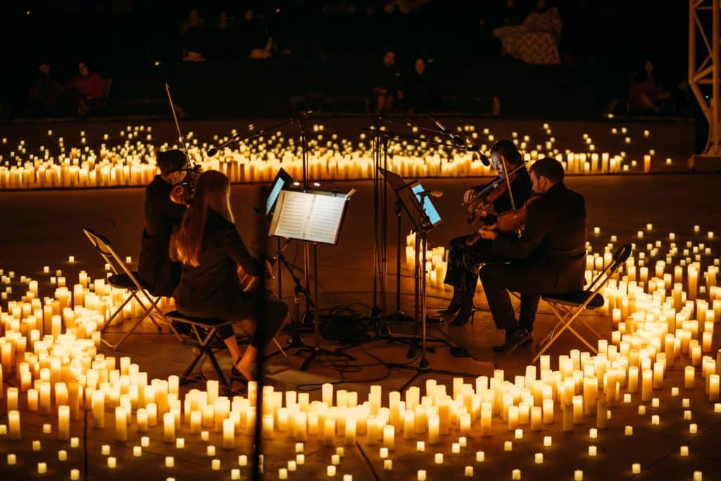 A string quartet performing in a circle surrounded by candles at an open-air Candlelight concert.