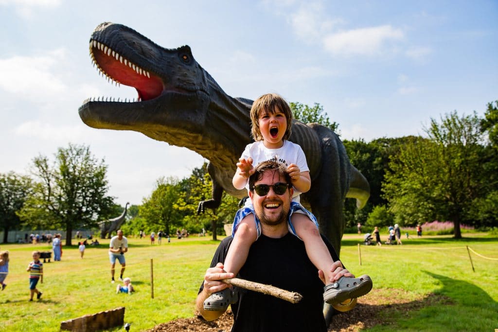 boy sits on shoulders of man with T-Rex animatronic in the background