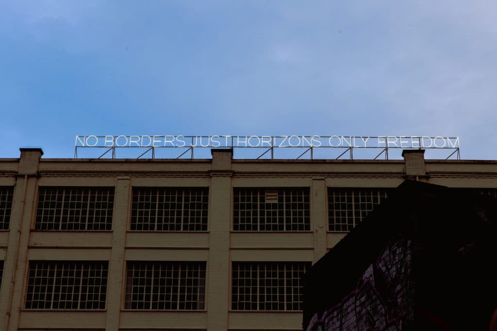 A neon sign on the roof of The Custard Factory that reads: No borders just horizons only freedom