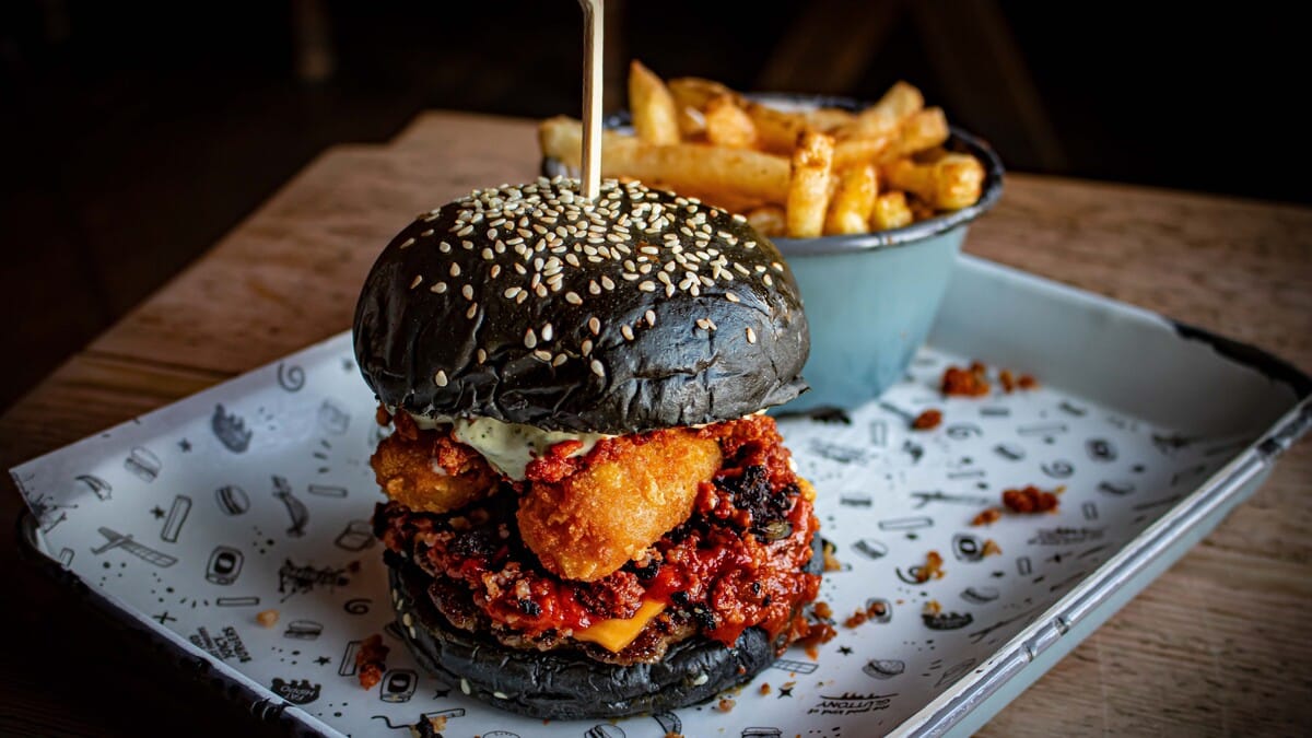 Fat Hippo's Hocus Porkus, a black bun beef burger with pork scratchings next to a bowl of chips