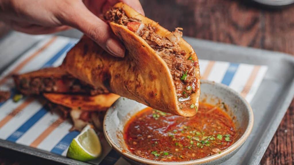 A birria taco held over some dipping sauce at The Watershed