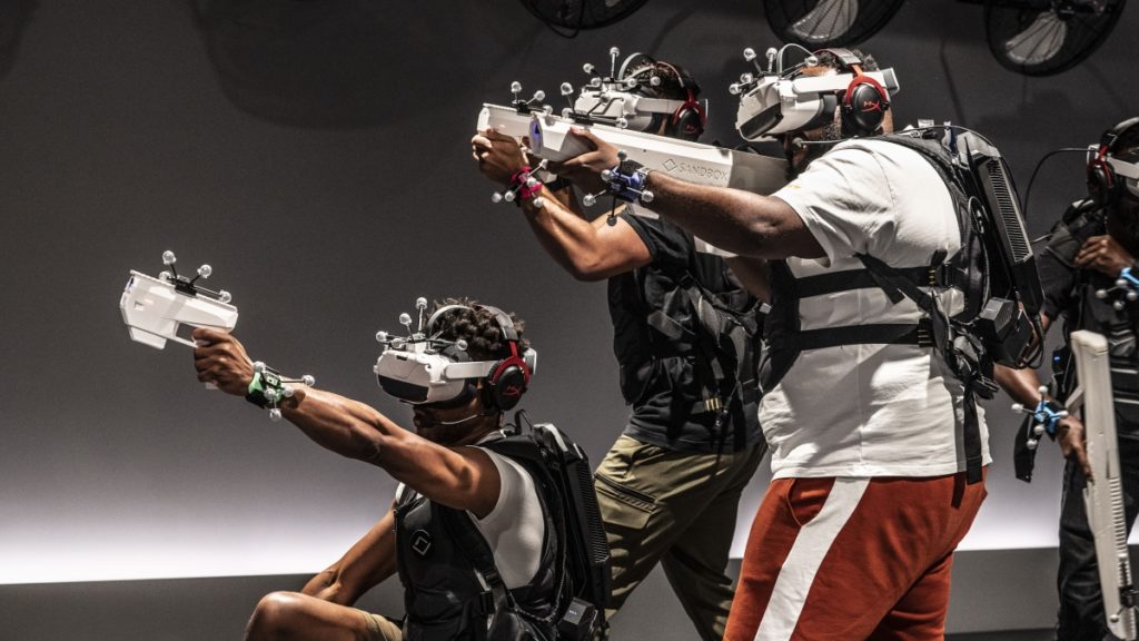 Three people at Sandbox VR wearing VR headsets and holding gaming guns