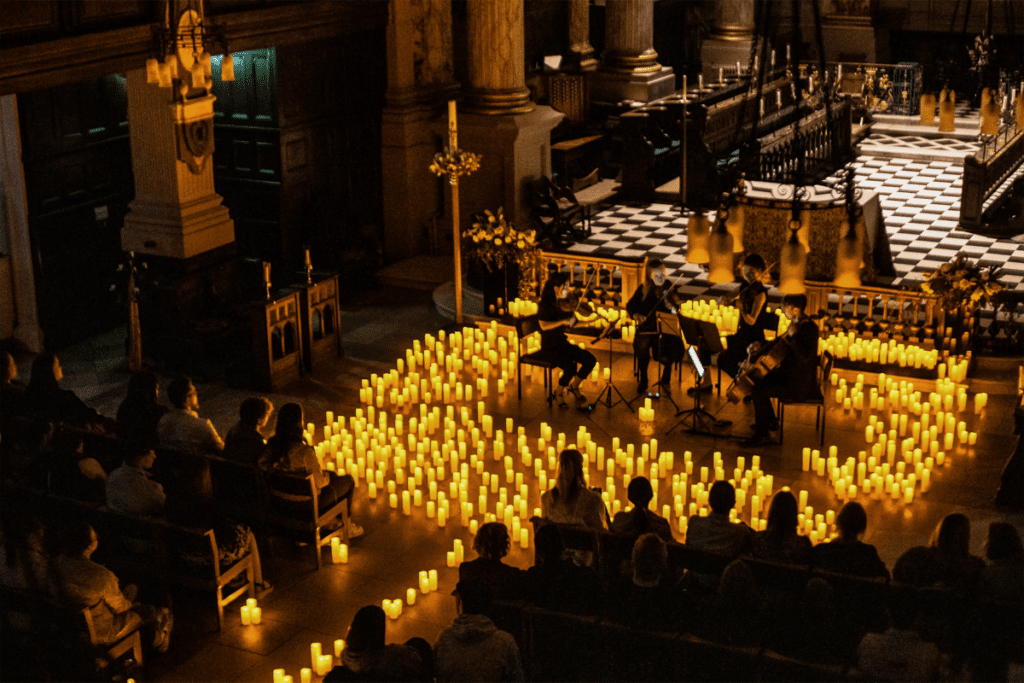 A string quartet performing inside Birmingham Cathedral surrounded by hundreds of flickering candles and the silhouette of the audience sitting in pews in front of them.