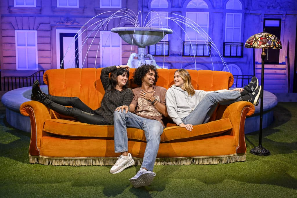 three friends sat on the iconic orange sofa at the Friends Experience in Paris