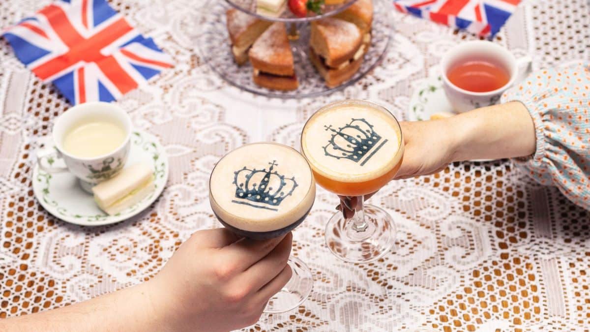 Two hands cheering limited edition King's Coronation Weekend cocktails surrounded by afternoon tea