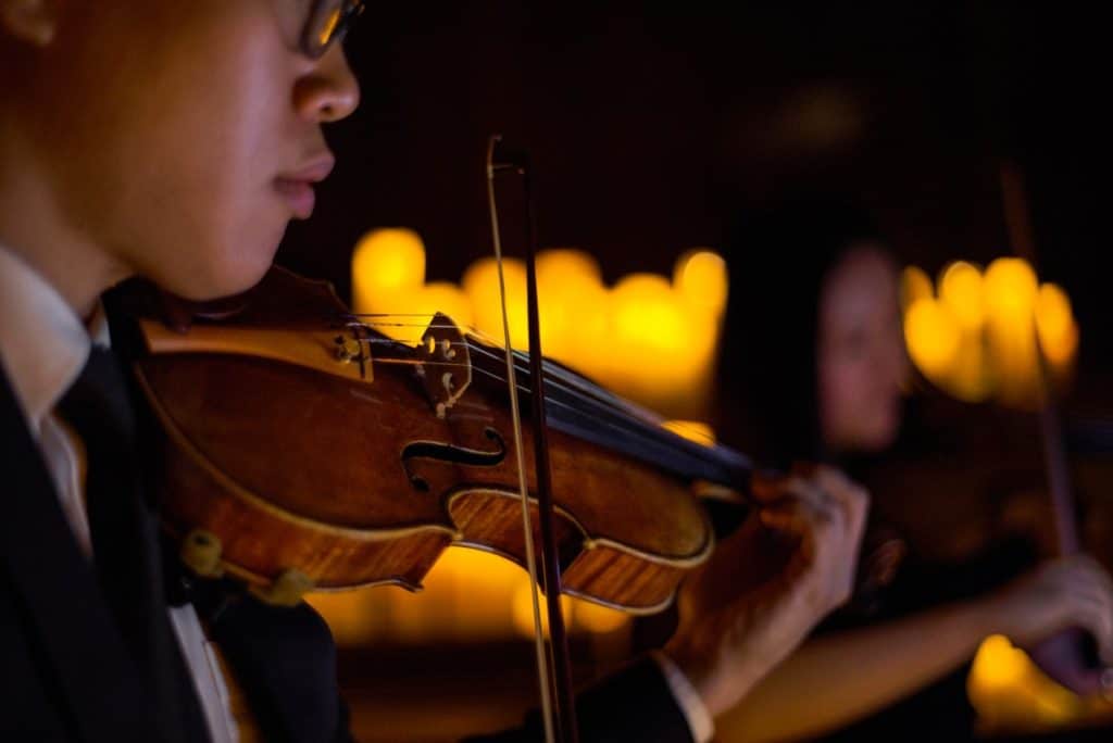 A close up of a violinist playing with candles in the background