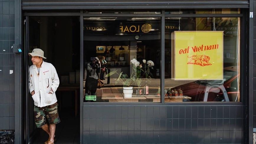 A man stood in the doorway of Vietnamese restaurant, with a yellow sign in the window, called Eat Vietnam. One of the best restaurants in Birmingham.