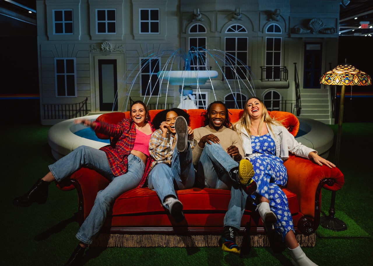 Four friends laughing on the iconic sofa in front of the fountain at The FRIENDS™ Experience