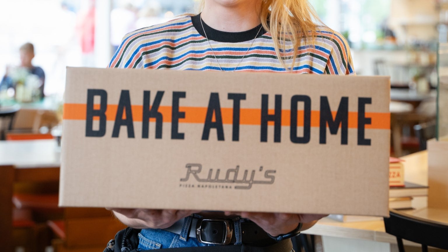 A woman holding a box of Rudy's Bake At home pizzas