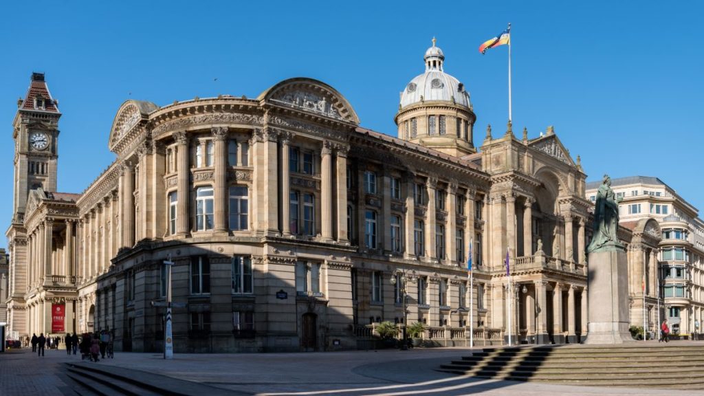 View of the Council House in Victoria Square with people enjoying the sunshine, Birmingham, with a flag flying from the roof