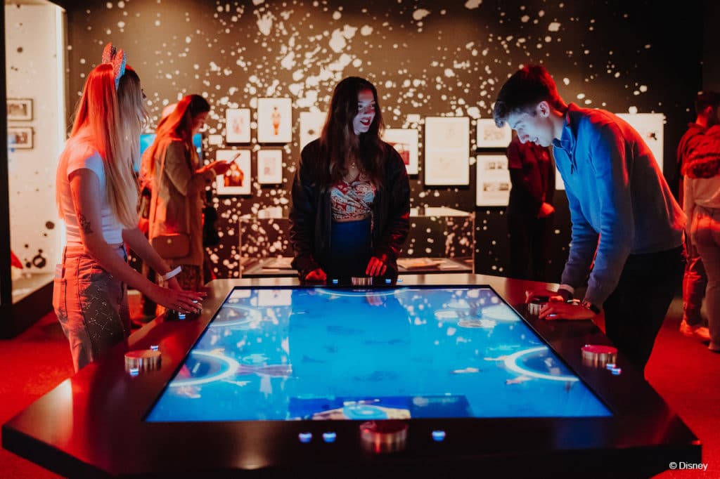 a group of friends surrounding an interactive table at Disney100: The Exhibition